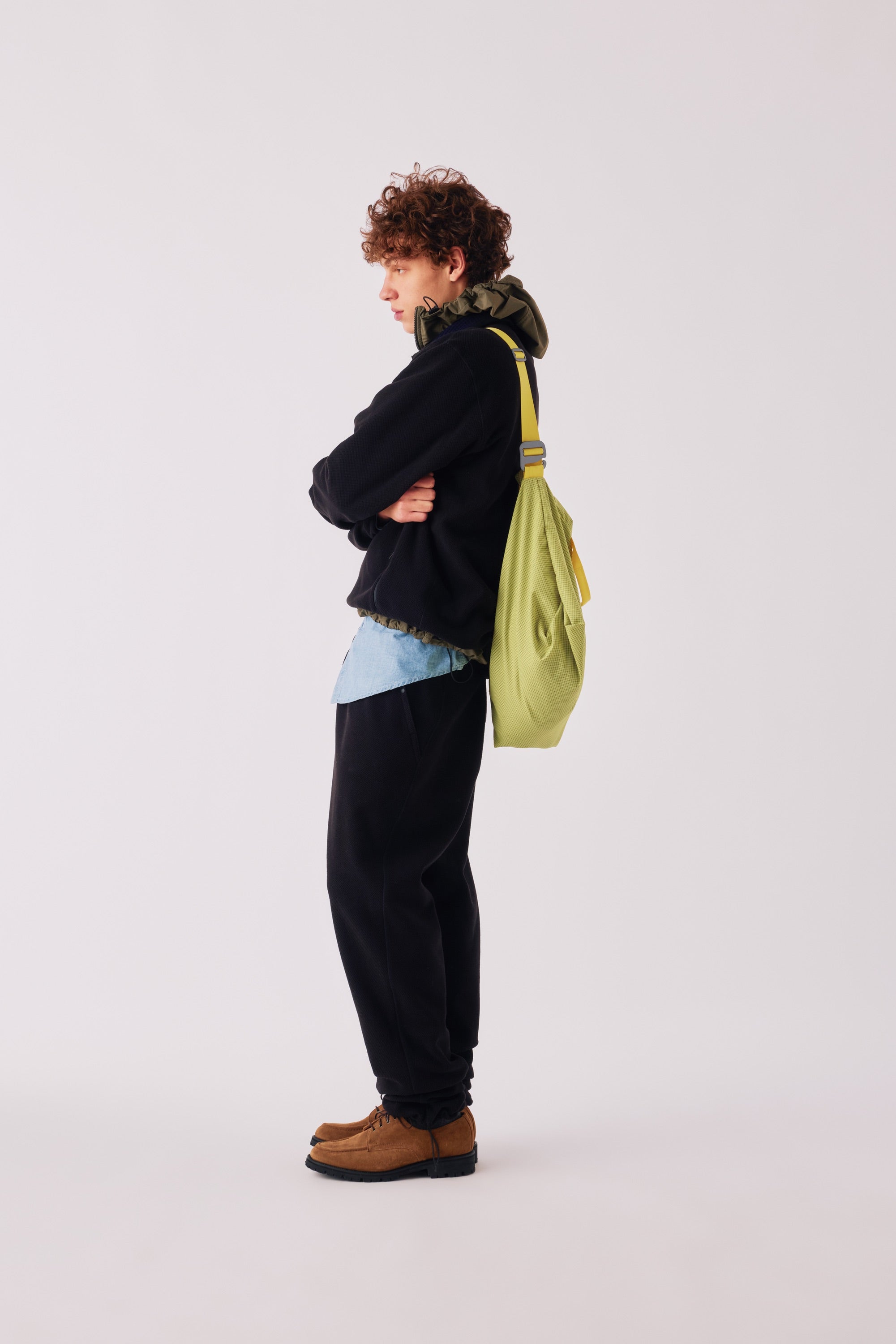 Adsum FW26 — model in a black fleece with a green sling bag, in profile